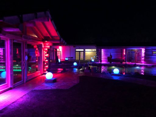 Bunte Beleuchtung eines modernen Außenbereichs mit Schwimmbecken bei Nacht.