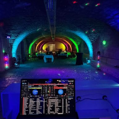 DJ-Pult in einem farbenfroh beleuchteten Veranstaltungssaal mit Bögen.