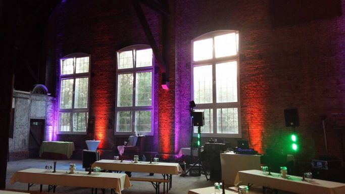 Ein heller Veranstaltungsraum mit bunten Lichtern und großen Fenstern.