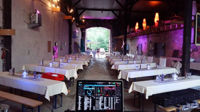 Innenansicht eines festlich dekorierten Veranstaltungsraums mit langen Tischen und bunten Lichtern.